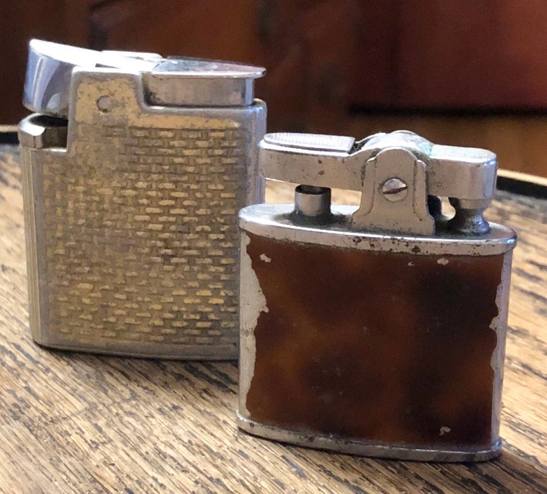 May include: Two vintage silver lighters. One lighter has a textured silver finish and the other has a brown plastic insert.