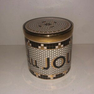 May include: A white ceramic jar with a black and gold mosaic design. The jar has the word "Du Jour" written in gold letters on the side.