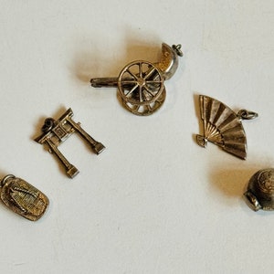 May include: Five silver charms depicting Japanese cultural elements: a fan, a gate, a rickshaw, a sandal, and a round jar.