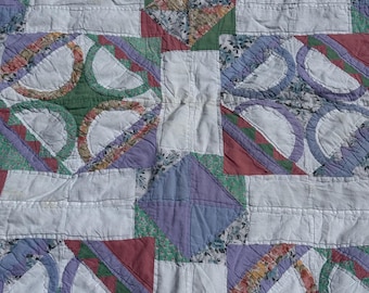 Puede incluir: Primer plano de un edredón hecho a mano con un diseño de patchwork. El edredón presenta un patrón repetitivo de formas de tela blanca, roja, verde, morada y floral. El edredón está hecho de tela acolchada suave.