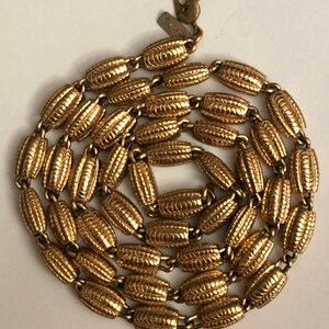 May include: A gold-tone chain necklace with a textured oval link design. The necklace has a lobster claw clasp and a small tag with the word "Monet" on it.