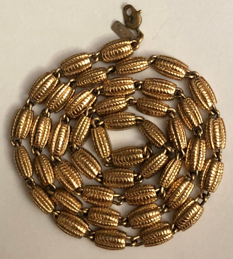 May include: A gold-tone chain necklace with a textured oval link design. The necklace has a lobster claw clasp and a small tag with the word "Monet" on it.