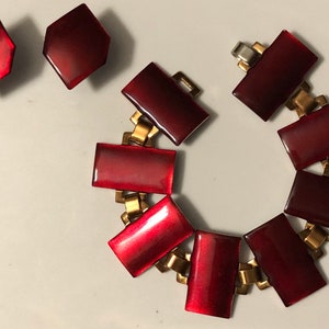 Peut inclure: Un bracelet en &eacute;mail rouge avec une cha&icirc;ne dor&eacute;e et une paire de boucles d'oreilles assorties. Le bracelet a des maillons de forme rectangulaire et les boucles d'oreilles sont hexagonales.