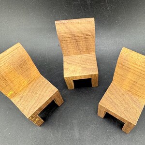 May include: Three small, wooden chairs with a natural wood grain finish. Each chair has a curved back and a rectangular base with a small, black opening. The chairs are arranged on a dark surface.