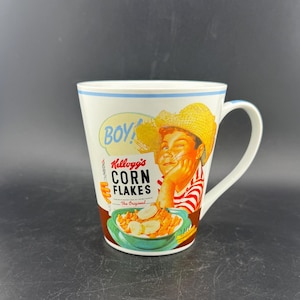 Może przedstawiać: Biały ceramiczny kubek z vintage'owym wzorem Kellogg's Corn Flakes. Kubek przedstawia uśmiechniętego chłopca w słomkowym kapeluszu, ze słowami "BOY!" i "Kellogg's Corn Flakes" wydrukowanymi z boku. Kubek ma niebieską obwódkę i uchwyt.