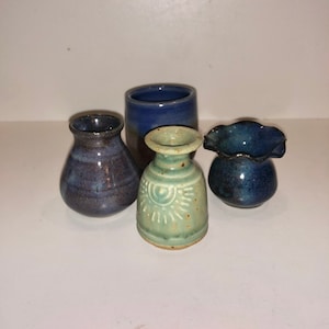 May include: Four small ceramic vases in different colors and designs. The vases are blue, green, and brown.
