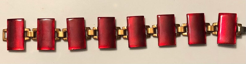 Peut inclure: Un bracelet en verre rouge avec des maillons en m&eacute;tal dor&eacute;. Le bracelet est compos&eacute; de pi&egrave;ces rectangulaires en verre rouge reli&eacute;es par des maillons en m&eacute;tal dor&eacute;.