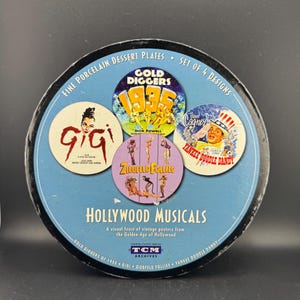 May include: Set of four fine porcelain dessert plates featuring vintage movie posters from the Golden Age of Hollywood. The plates feature images from "Gold Diggers of 1935", "Gigi", "Ziegfeld Follies", and "Yankee Doodle Dandy".