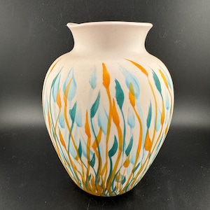 以下が含まれることがあります： 緑とオレンジの抽象的な花柄が手描きされた白い陶器の花瓶