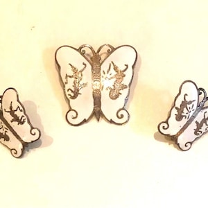 May include: A set of three silver butterfly earrings and a brooch. The butterflies are white with black outlines and have a delicate design.