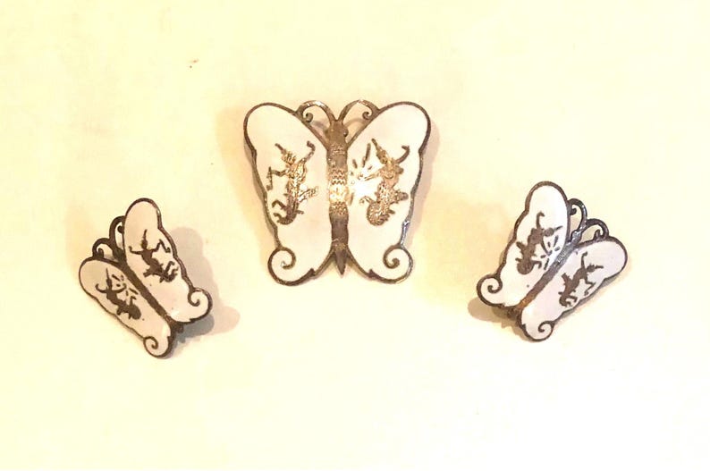 May include: A set of three silver butterfly earrings and a brooch. The butterflies are white with black outlines and have a delicate design.