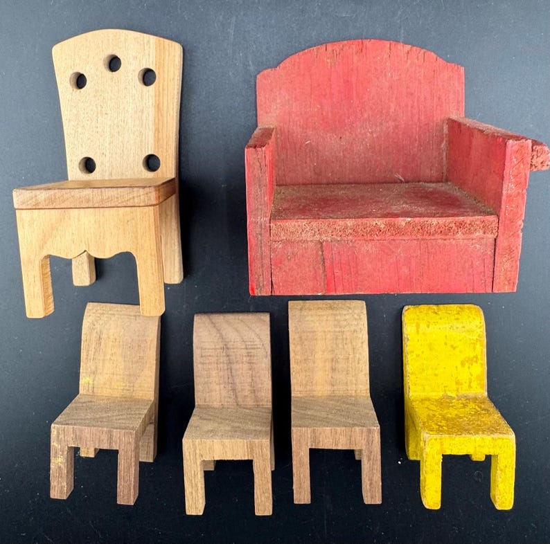 May include: A collection of miniature wooden furniture pieces, including a light-colored chair with a perforated back, a red armchair, and several small chairs in shades of brown and yellow. The pieces are arranged on a dark surface.