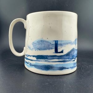 Peut inclure: Une tasse en c&eacute;ramique blanche avec une anse noire et le texte "But First, Coffee" en gras noir. La tasse est pos&eacute;e sur un fond flou. La tasse mesure environ 10 cm de hauteur.