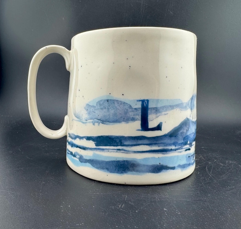Peut inclure: Une tasse en c&eacute;ramique blanche avec une anse noire et le texte "But First, Coffee" en gras noir. La tasse est pos&eacute;e sur un fond flou. La tasse mesure environ 10 cm de hauteur.