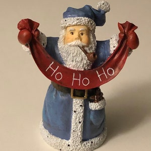May include: A blue and white Santa Claus figurine holding a red banner that says "Ho Ho Ho".