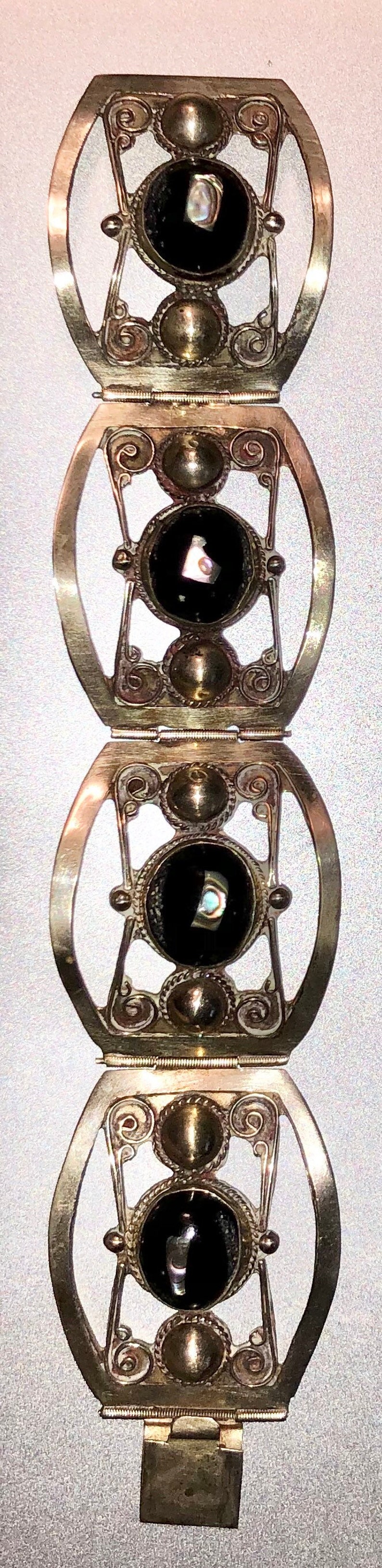 Puede incluir: Pulsera plateada con cuatro eslabones ovalados con dise&ntilde;os de filigrana ornamentados. Cada eslab&oacute;n tiene una piedra negra central con acentos iridiscentes. Cierre de broche, probablemente vintage.