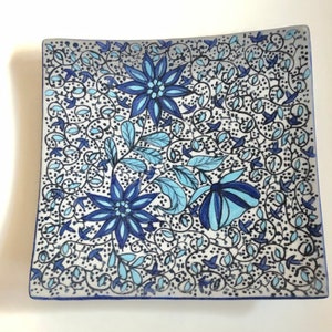May include: A square ceramic plate with a blue and white floral design. The plate features intricate patterns of flowers, leaves, and vines.