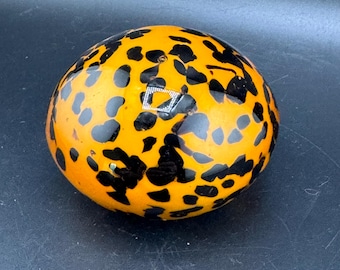 May include: A round, orange glass paperweight with a black leopard print pattern.
