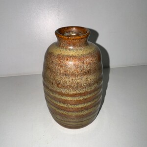 以下が含まれることがあります： ストライプ模様の茶色とベージュの陶器の花瓶。花瓶は丸みを帯びたボディと狭い開口部を持っています。