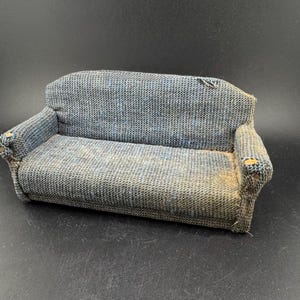 May include: A miniature blue and gray fabric sofa with armrests. The small couch has a woven texture and appears to be vintage. The sofa is a dollhouse furniture item.