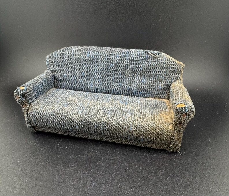 May include: A miniature blue and gray fabric sofa with armrests. The small couch has a woven texture and appears to be vintage. The sofa is a dollhouse furniture item.