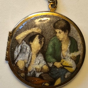 May include: A round, hinged pendant necklace with a gold-tone frame and a silver chain. The pendant features a painted scene of two figures in a room, with one wearing a green jacket. The pendant is approximately 1.5 inches in diameter.