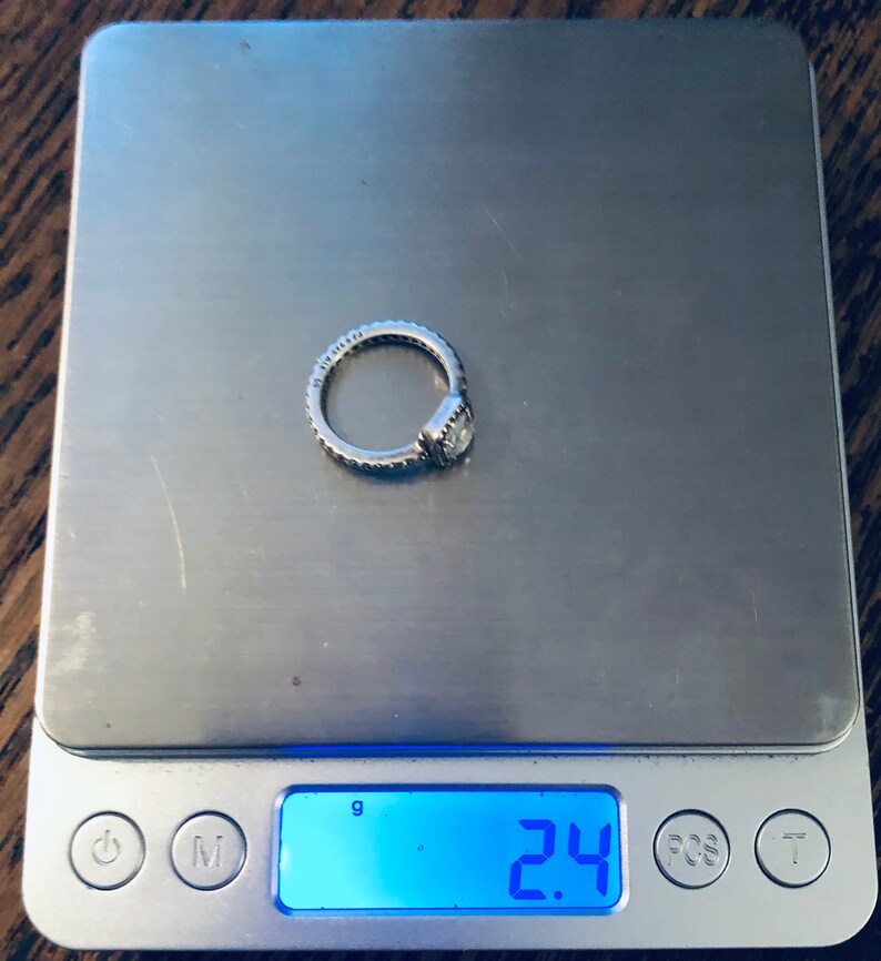 May include: A silver ring with a clear stone on a digital scale that reads 2.4 grams.
