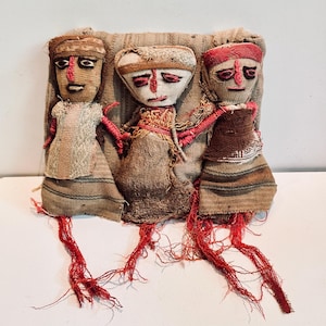 Puede incluir: Tres muñecas de tela hechas a mano con caras bordadas y pelo de hilo rojo. Las muñecas llevan ropa sencilla de tela marrón y blanca y están dispuestas en fila.