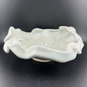 May include: A white ceramic bowl with a wavy, organic shape. The bowl has a textured surface and a slightly glazed finish.