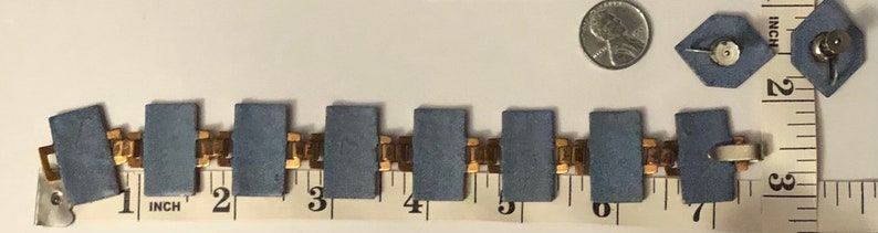 Peut inclure: Un bracelet en cha&icirc;ne dor&eacute;e avec des maillons rectangulaires bleus, mesur&eacute; sur une r&egrave;gle en pouces. Le bracelet mesure 7 pouces de long.