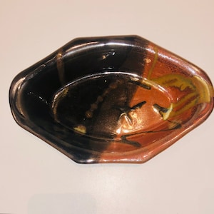 May include: A brown, black, and orange ceramic serving dish with a slightly oval shape and a textured glaze.