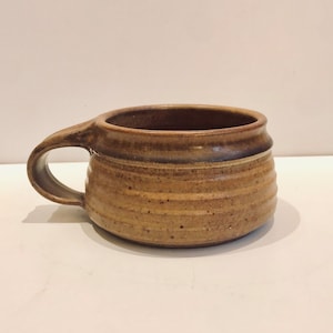 May include: A brown ceramic mug with a rounded shape and a handle. The mug has a textured, slightly speckled surface.