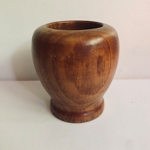 May include: A wooden mortar and pestle, made of dark brown wood. The mortar is round and has a wide base. The pestle is long and slender.