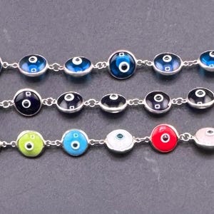 Pode incluir: Três pulseiras de prata com amuletos coloridos de olho grego. As pulseiras apresentam cores azul, preto e um arco-íris de cores, incluindo vermelho, verde e amarelo. Cada amuleto tem uma íris branca e uma pupila preta.