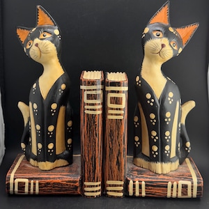 Peut inclure: Paire de serre-livres en bois en forme de chats. Chaque chat est noir avec des oreilles orange et des détails jaunes. Les serre-livres sont conçus pour maintenir des livres.