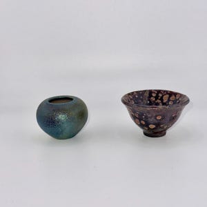 May include: Two small ceramic bowls, one is a dark green with a speckled finish, the other is a dark brown with a speckled finish and white spots.