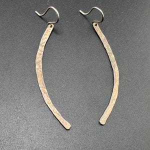 May include: A pair of silver hammered earrings with a curved shape and a simple wire hook closure.