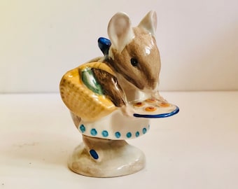 May include: A ceramic figurine of a mouse carrying a basket and a plate of treats. The mouse is brown and white, wearing a blue bow and a white apron with blue dots. The basket is tan and green.