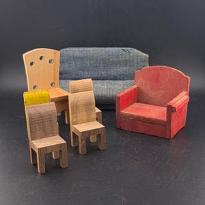 May include: A collection of miniature wooden furniture, including chairs and a sofa. The chairs are in various styles and colors, with one red armchair and a blue fabric sofa in the background. The furniture is likely for a dollhouse.