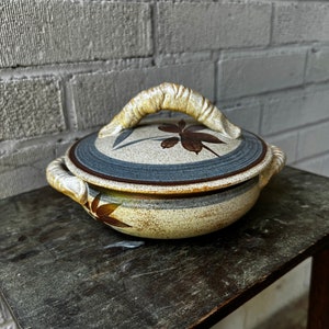 Peut inclure: Un plat de service en céramique avec un motif floral brun et blanc. Le plat a un couvercle avec une poignée et est fait dans un style rustique.