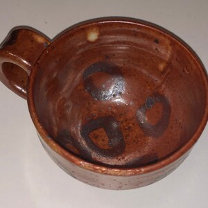 May include: A brown ceramic mug with a handle. The mug has a speckled glaze and dark brown markings.
