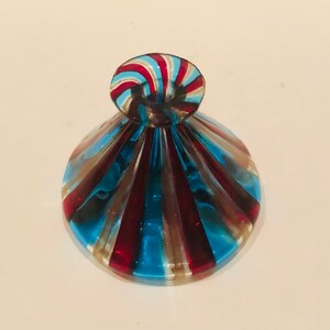 May include: A decorative glass bottle stopper with a spiral top. The stopper has alternating red, blue, and gold stripes. The base is a rounded shape with similar coloured stripes.