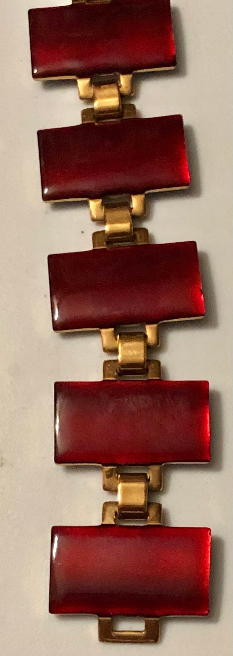 Peut inclure: Un bracelet rouge et or avec des pierres rouges rectangulaires et des maillons dor&eacute;s.
