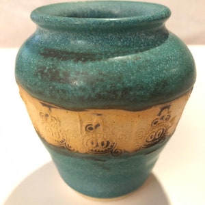 May include: A small, teal-coloured ceramic vase with a brown rim and a band of beige with a repeating pattern of stylised owls around the middle.
