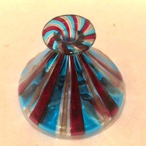 May include: A decorative glass object with a flared base and a rounded top. The glass features alternating stripes of blue, red, and white. The top has a spiral design with the same colour scheme. The object appears to be a decorative piece.