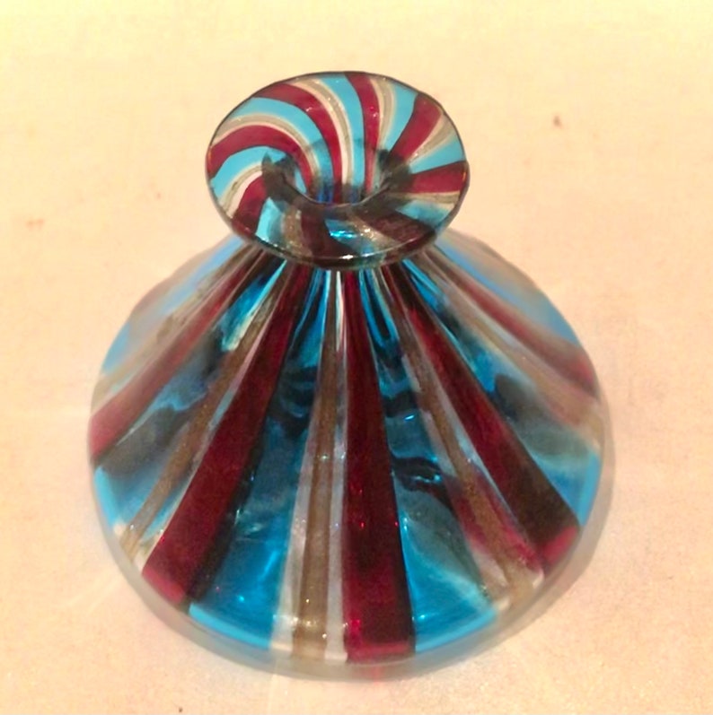 May include: A decorative glass object with a flared base and a rounded top. The glass features alternating stripes of blue, red, and white. The top has a spiral design with the same colour scheme. The object appears to be a decorative piece.