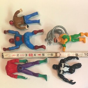 May include: Five action figures of superheroes, including Spider-Man, Venom, and Doc Ock. The figures are made of plastic and are painted in various colors, including red, blue, green, black, and yellow. The figures are posed in action poses and are ready for battle.