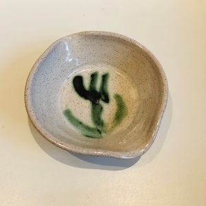以下が含まれることがあります： 斑点のある釉薬をかけた小さな白い陶器のボウル。ボウルは内側に緑と黒の抽象的なデザインが施されています。