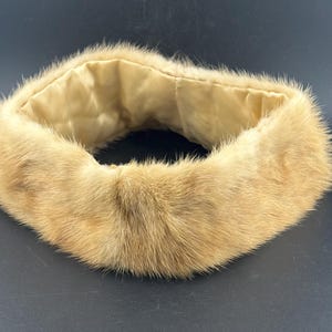 May include: A light brown fur collar with a soft, light-coloured lining. The fur appears to be in good condition, with a dense and plush texture. The collar is circular and designed to be worn around the neck.
