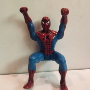 May include: A red and blue plastic action figure of Spider-Man with his arms raised in the air. The figure is posed in a dynamic action pose.